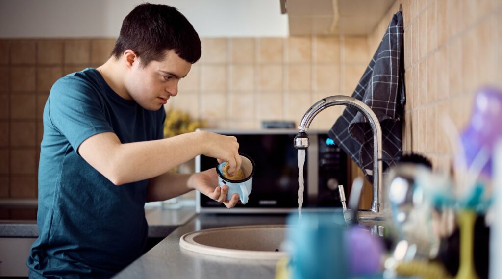 Young down syndrome man washing dishes